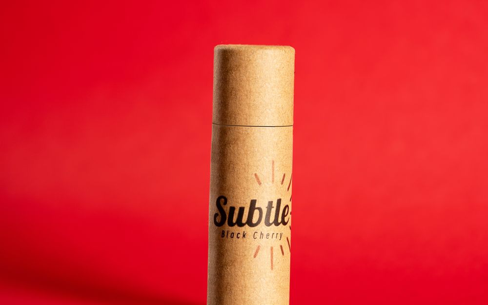 A Subtle lip balm tube in Black Cherry on a red backdrop